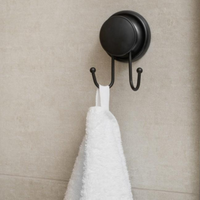 Compact matte black double hook mounted on a smooth tiled wall
