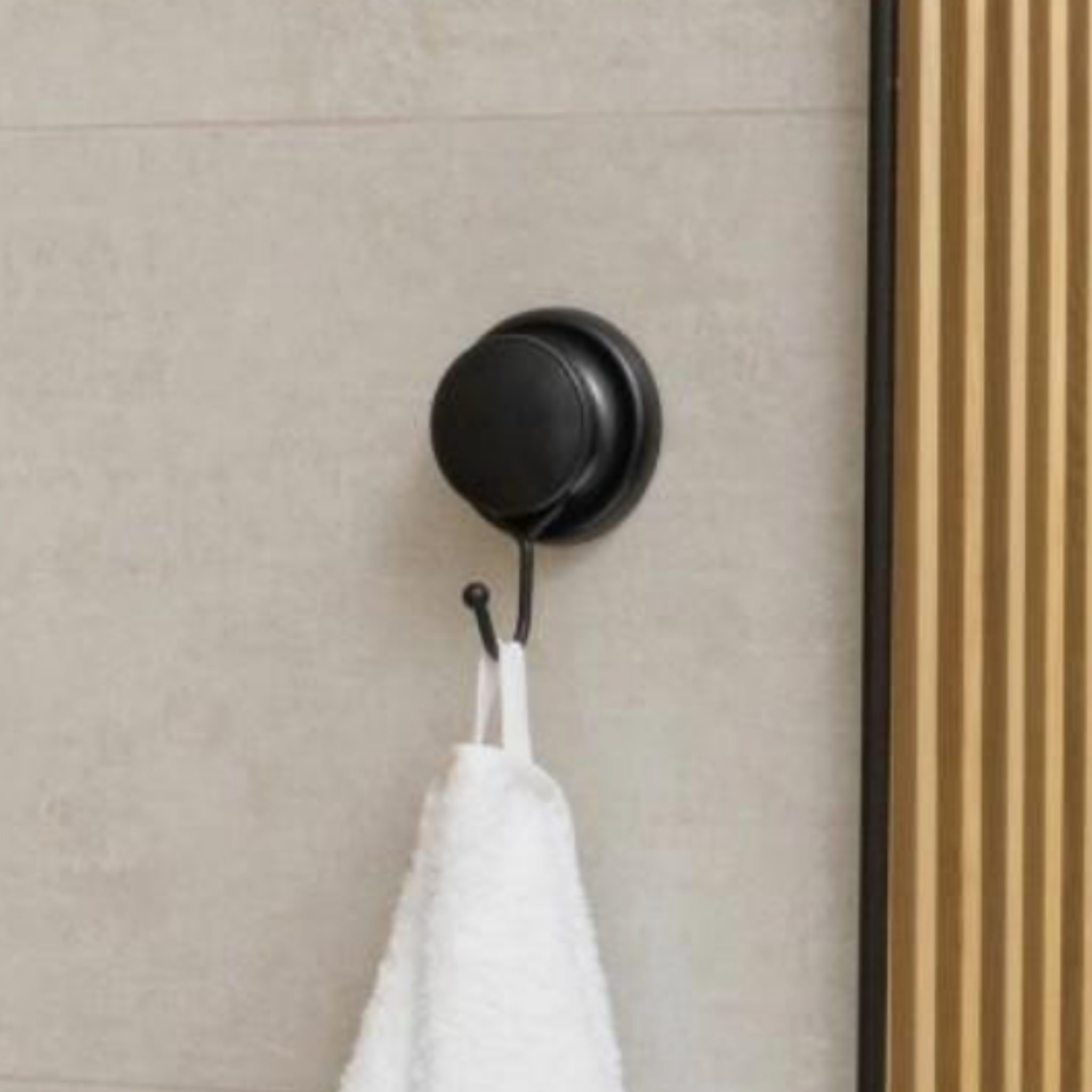 Matte black self-adhesive towel hook mounted on a smooth tiled wall