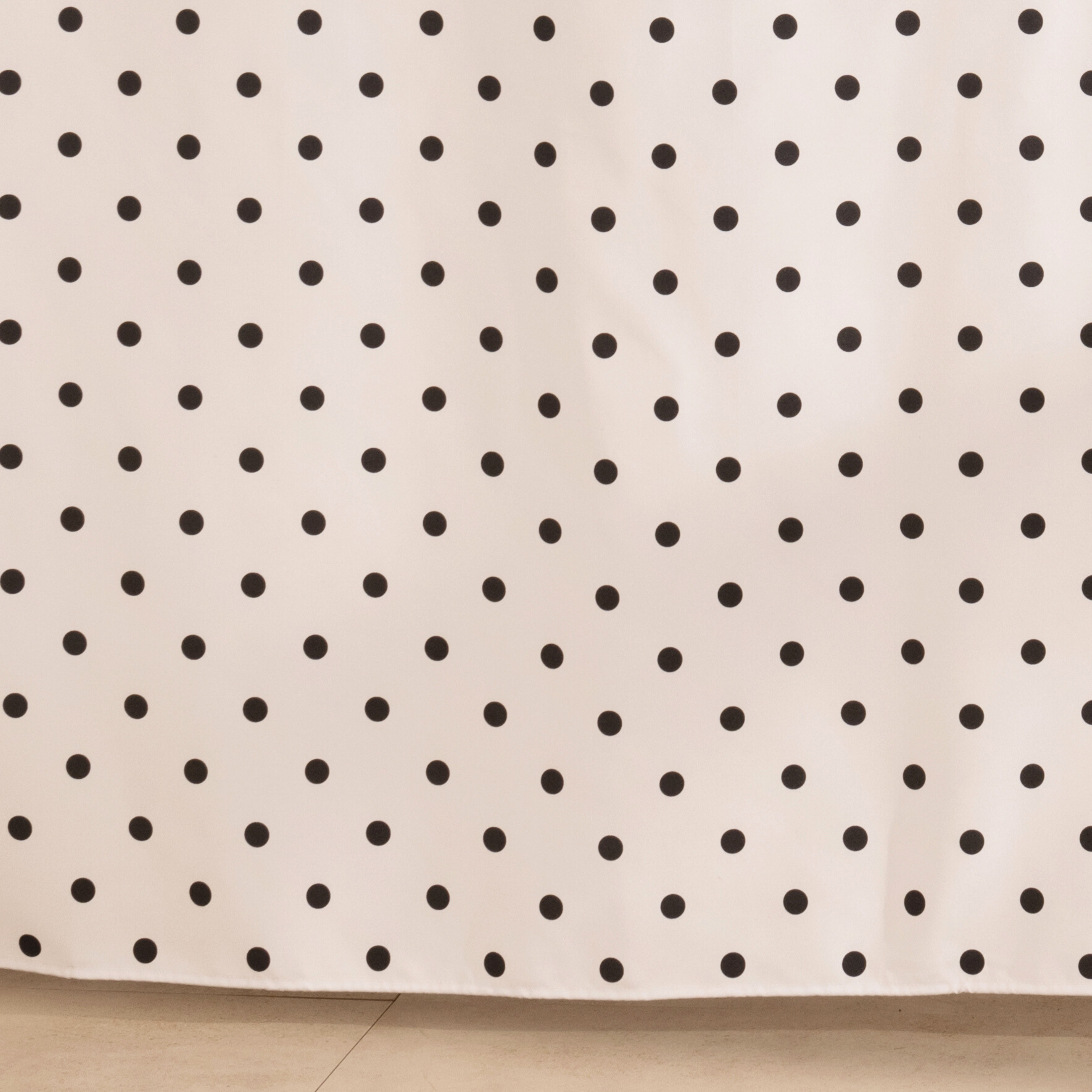 Full length dotted beige curtain hanging beside a glass screen