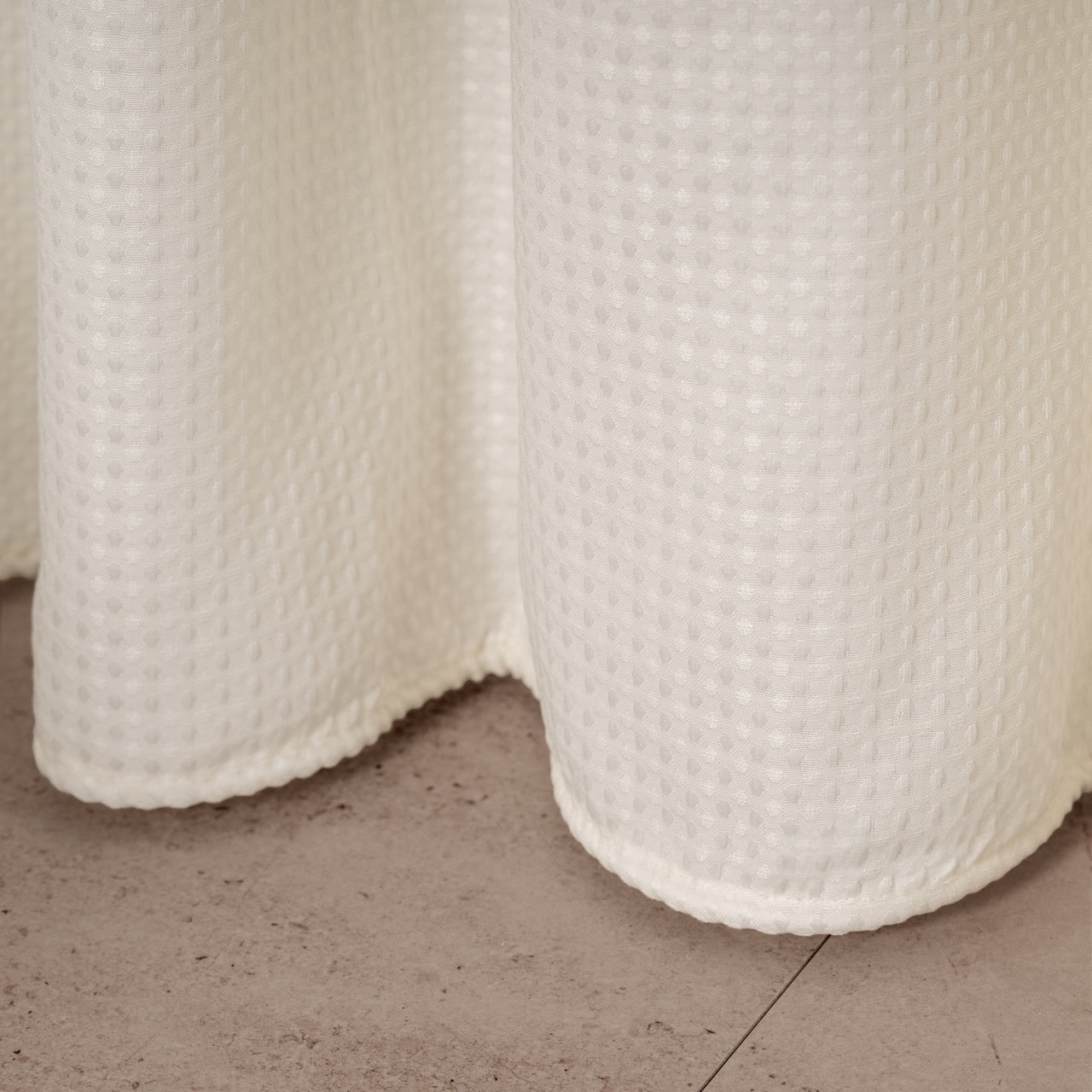 Full length cream waffle curtain hanging beside a glass screen