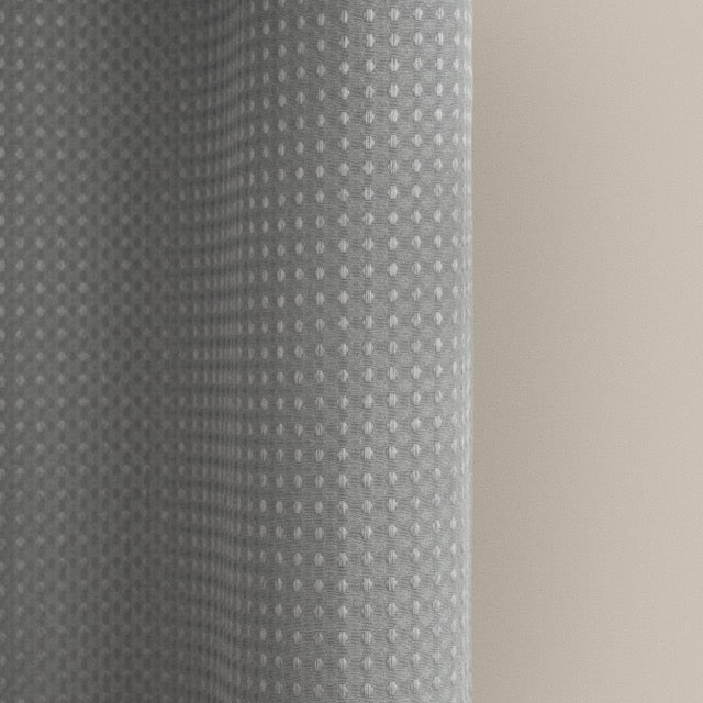 Full length grey waffle curtain hanging beside a glass shower screen