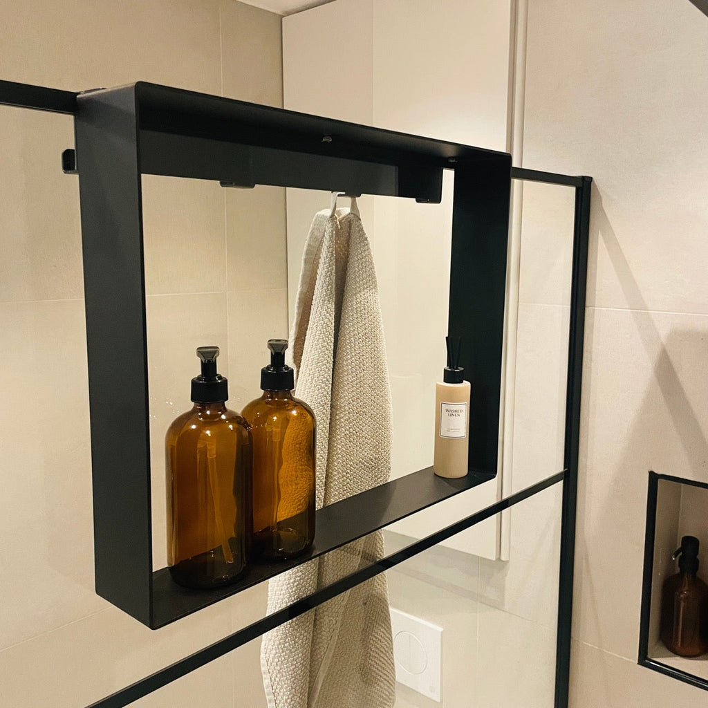 Black double-sided caddy hooked over a glass shower screen holding bottles