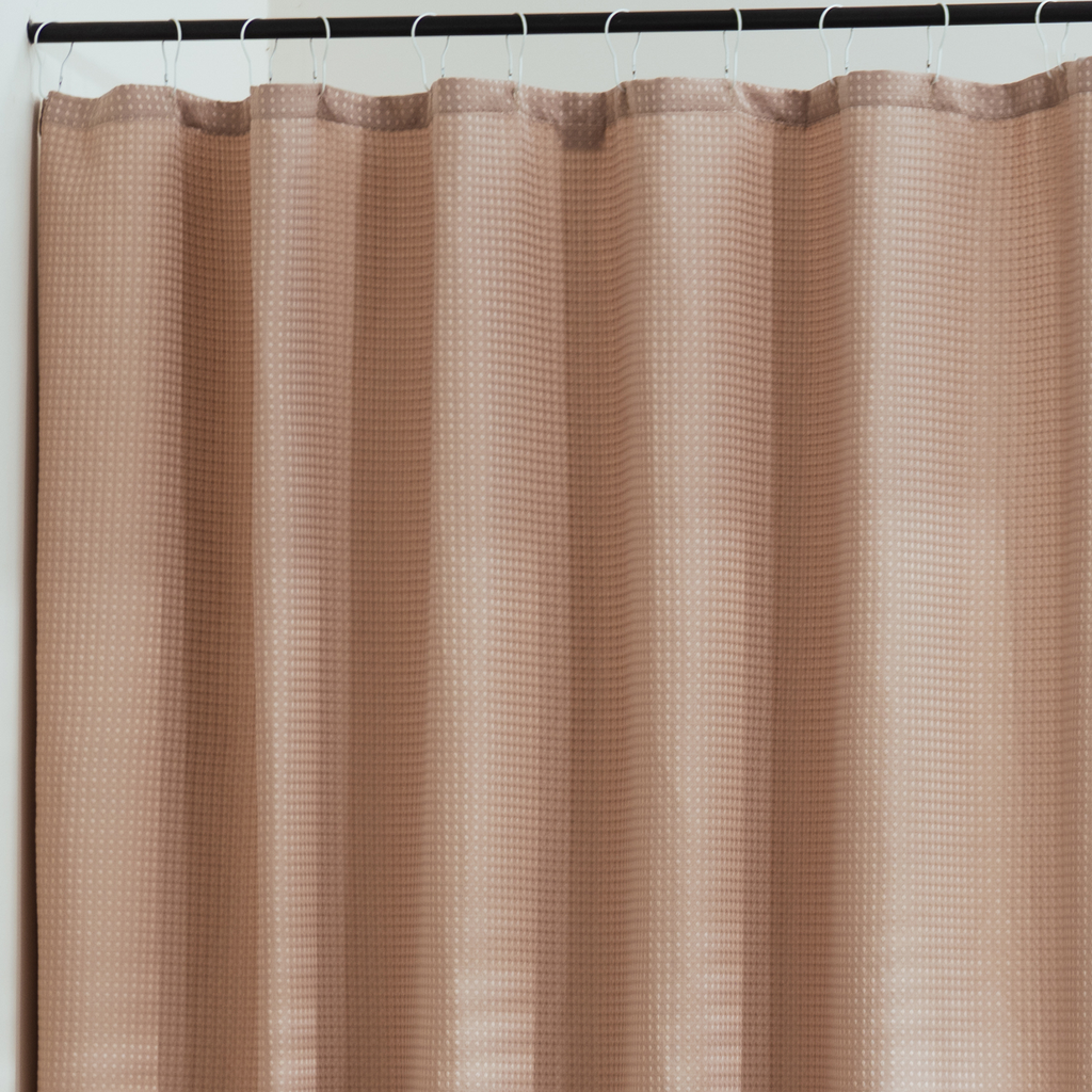 Full length nude beige curtain hanging beside a glass shower screen