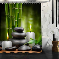Green bamboo behind a stack of polished black stones and two lit candles