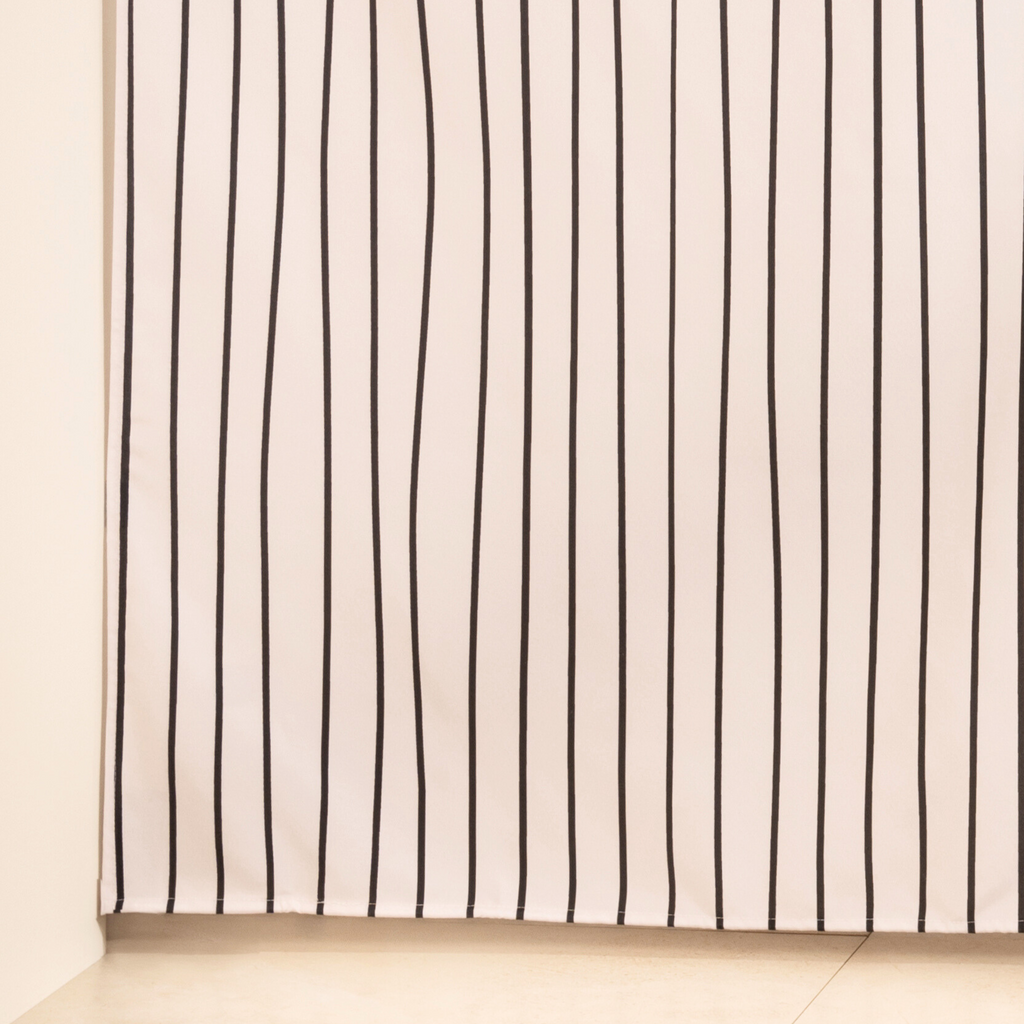 Full length striped curtain hanging beside a glass shower screen