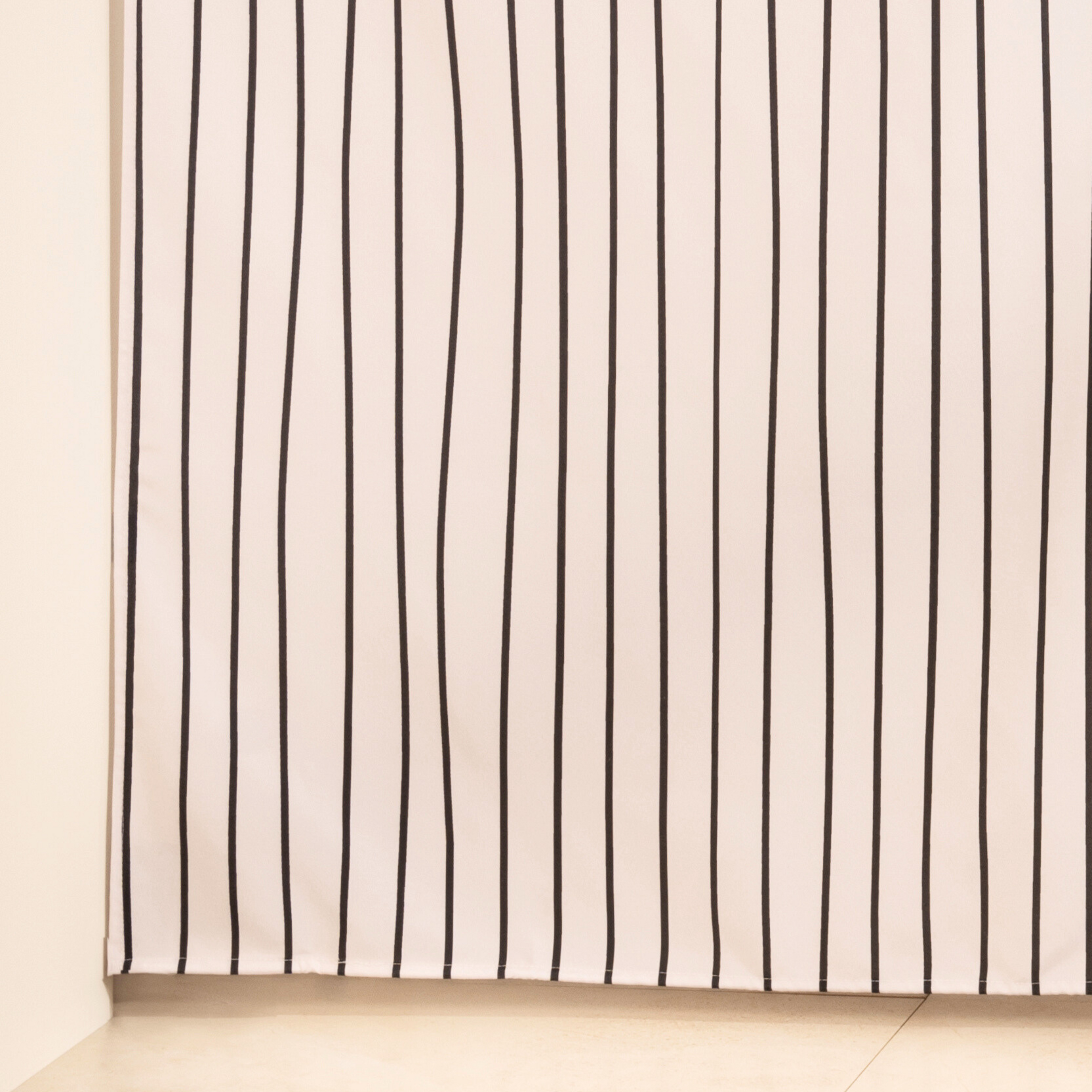 Full length striped curtain hanging beside a glass shower screen