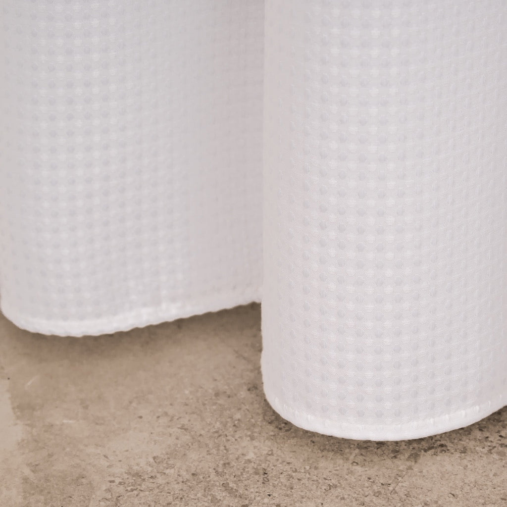 Full length white waffle curtain hanging beside a glass screen